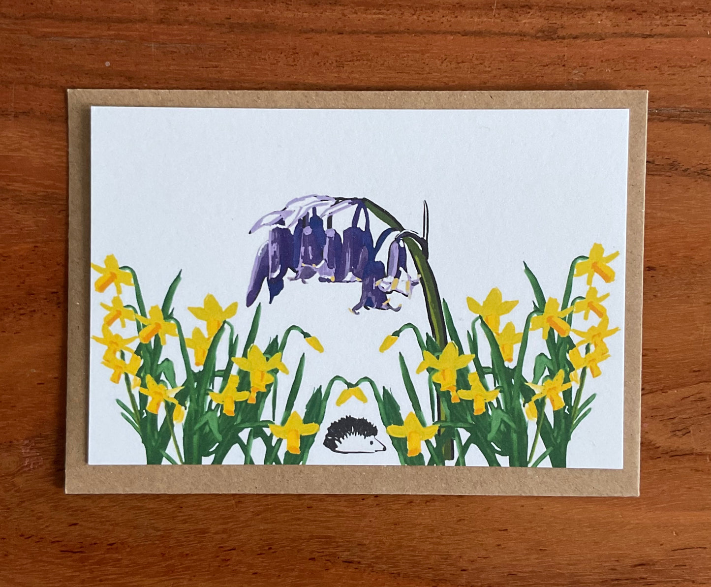 Close-up of wild notecard showing detailed hand-drawn bluebells, daffodils and hedgehog illustrations on premium 350gsm recycled cardstock texture.
